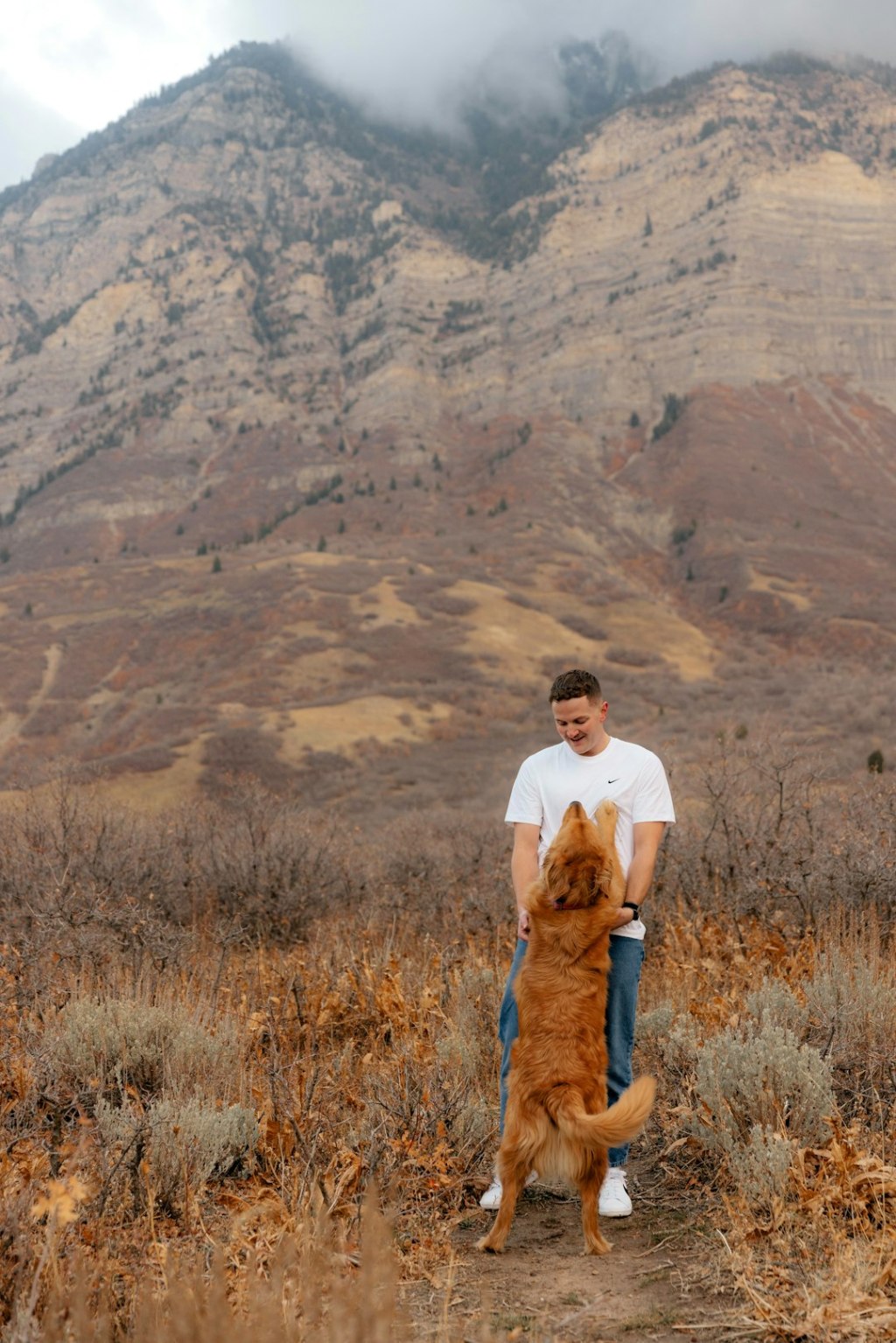 Man holding a golden retriever dog outdoors with mountains behind